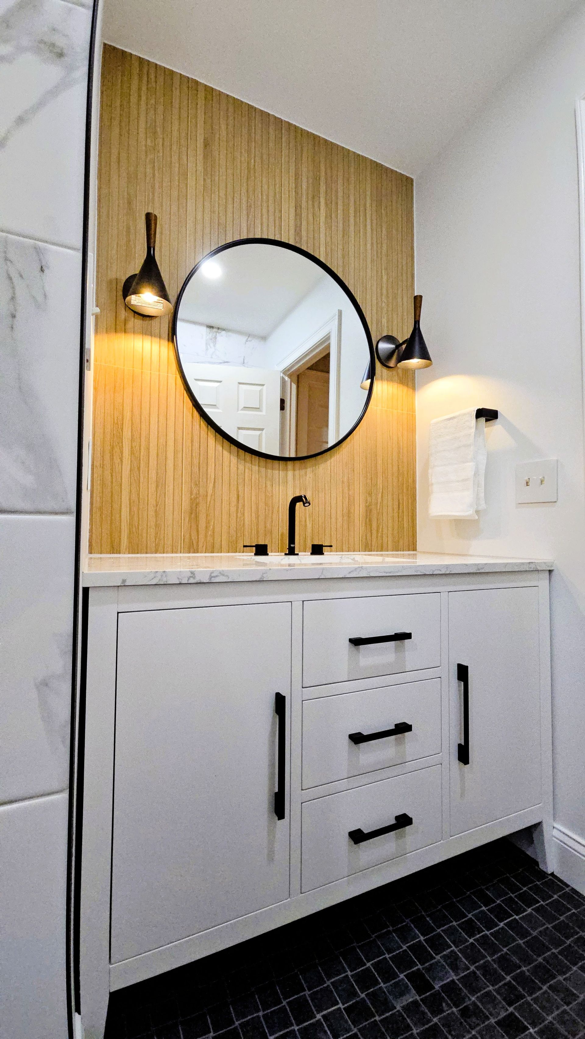Newington bathroom with white vanity, black hardware, round mirror, and wood accent wall.