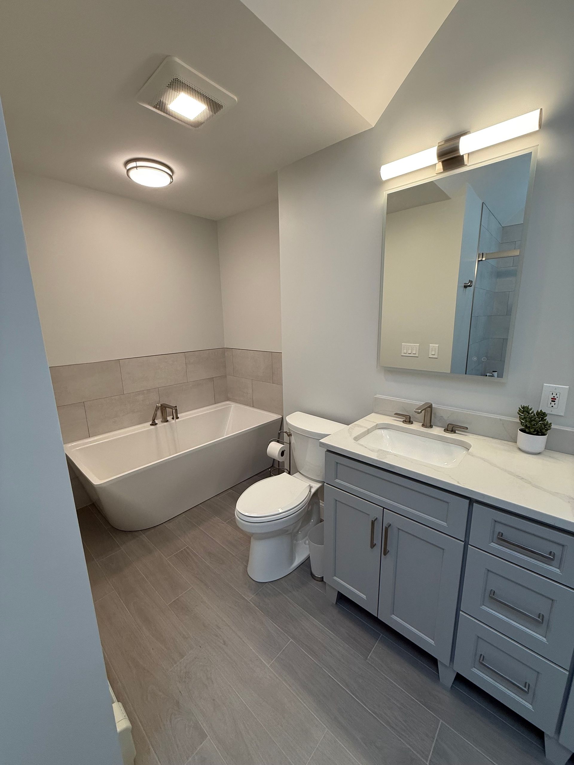 A bathroom with a tub , toilet , sink and mirror.