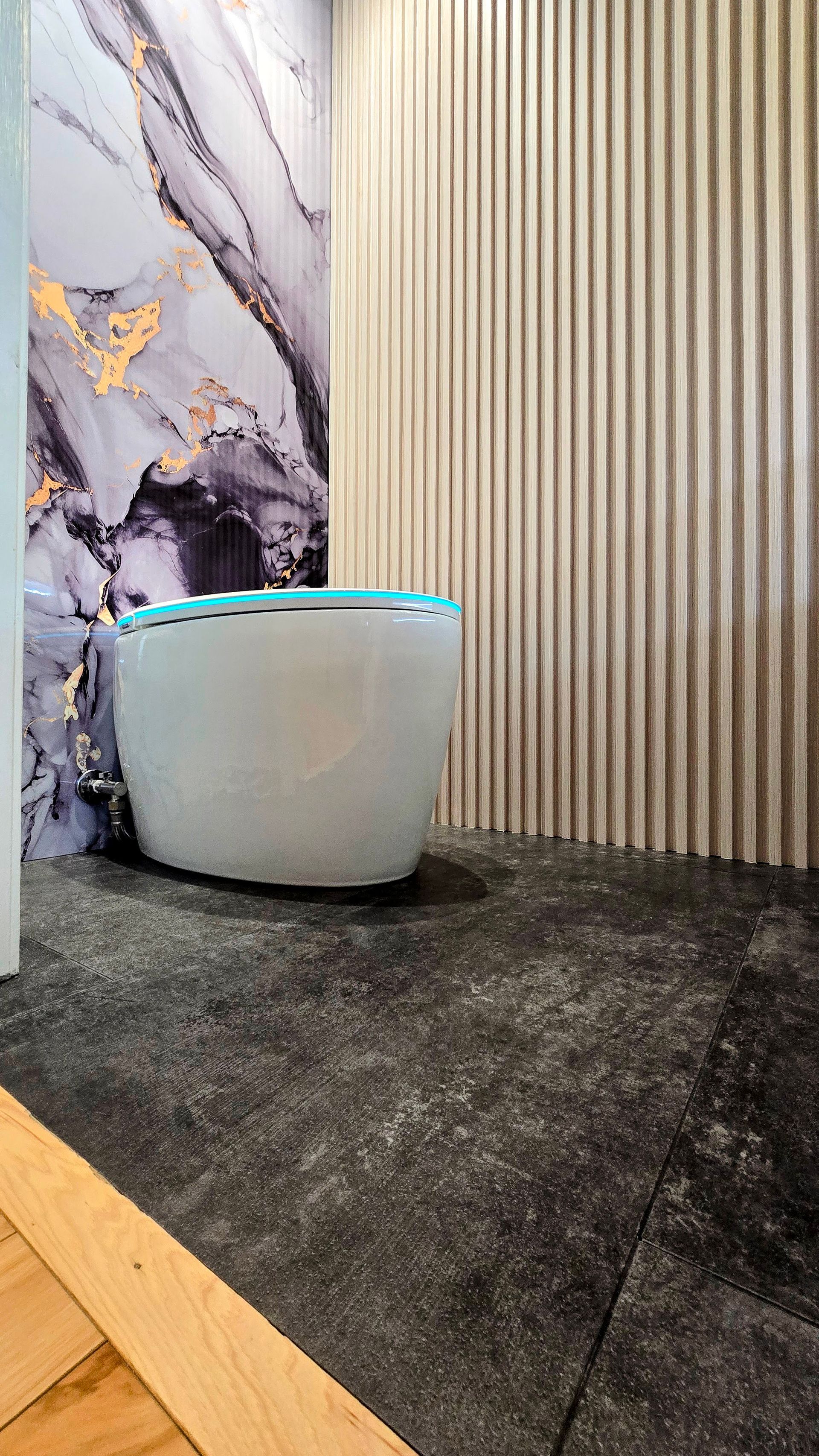 Toilet in modern bathroom in Simsbury, CT with marble and textured walls. Dark gray floor and wood trim.