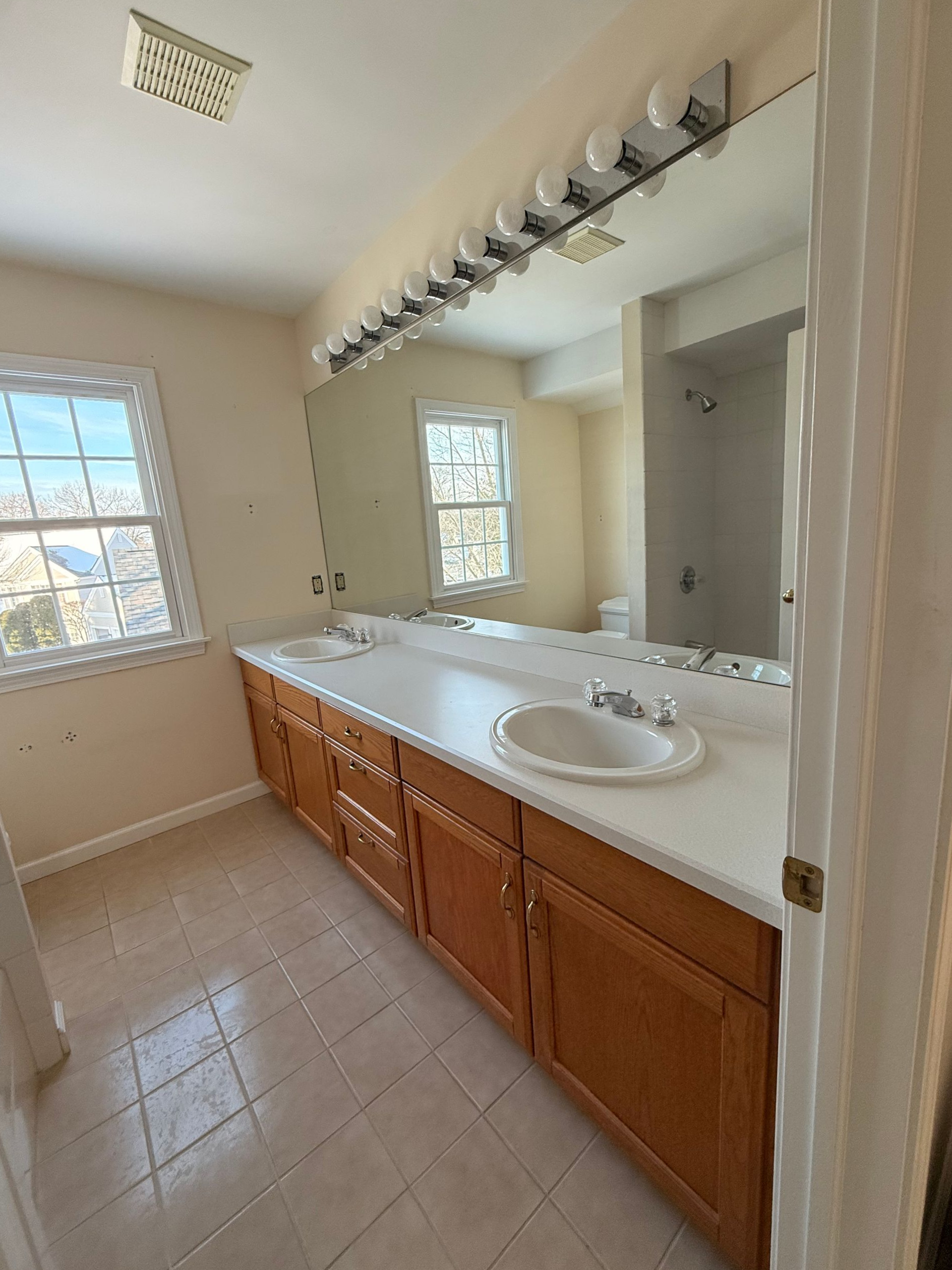A bathroom vanity in Cromwell, CT with wood cabinets, a white countertop with a sink, and a large mirror with a row of lights above.