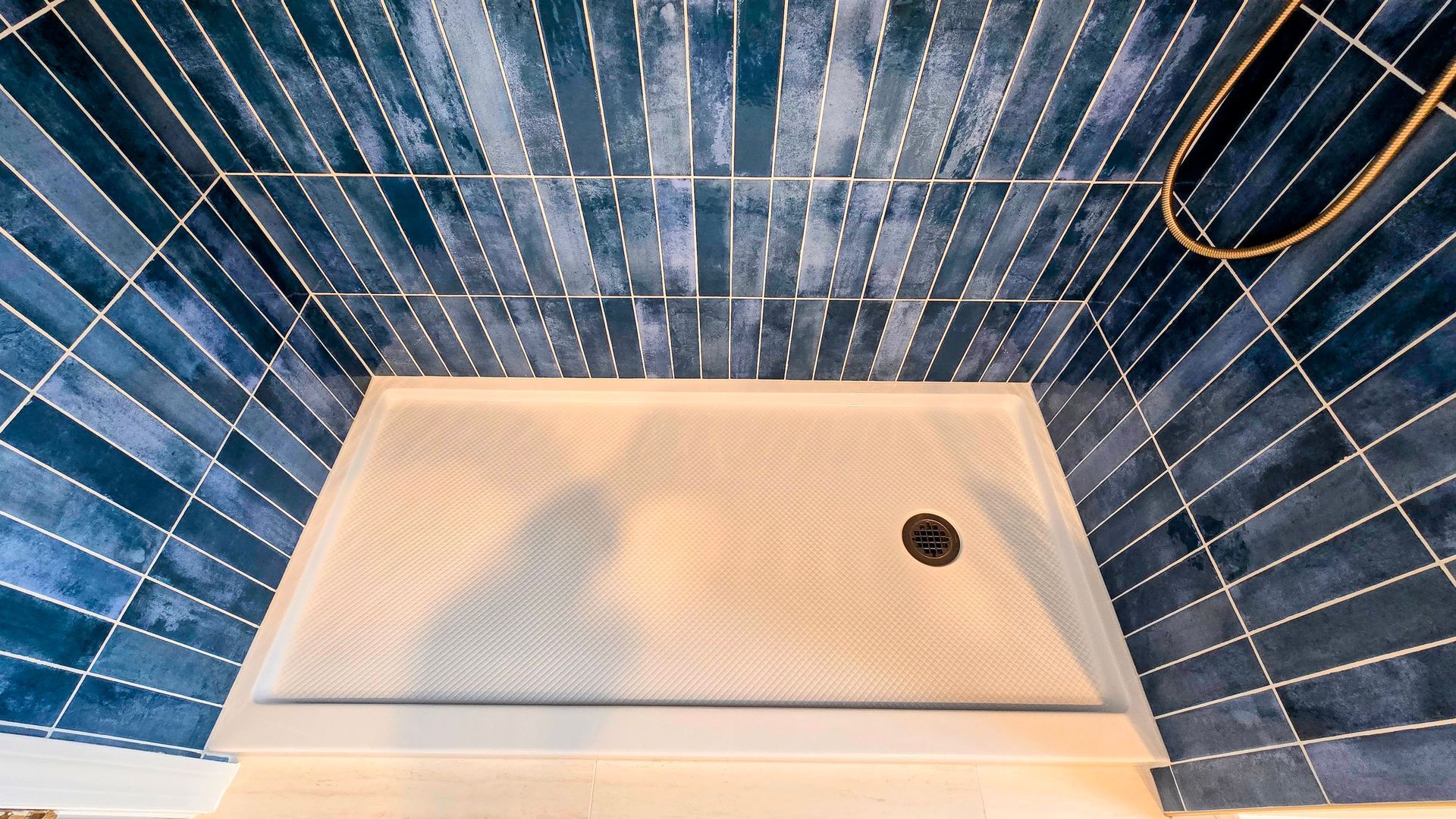 A modern shower stall in Cromwell, CT featuring a textured light beige floor and vertical deep blue glossy subway tiles on the walls.