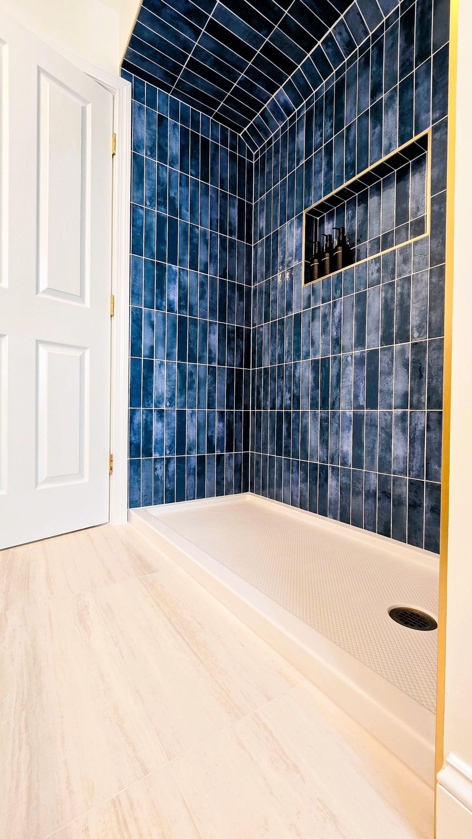A modern shower with deep blue, vertically stacked tiles, a gold-trimmed recessed niche, and a light-toned floor.