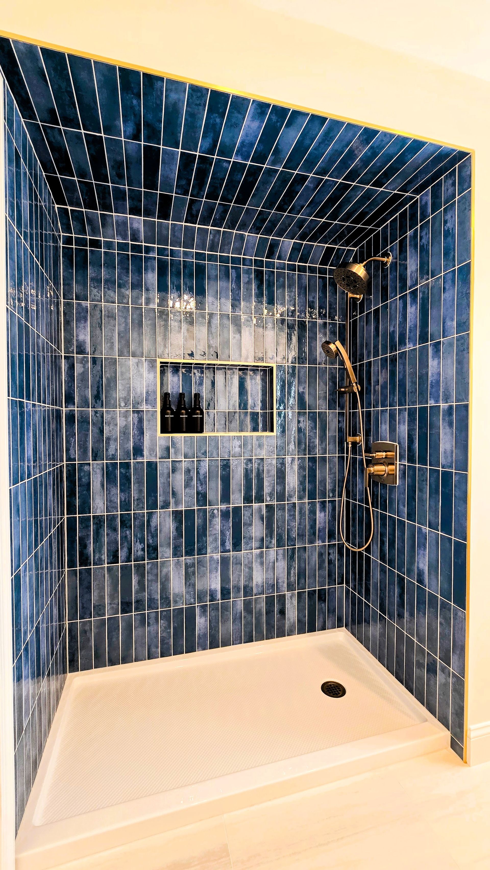 A walk-in shower in Cromwell, CT with deep blue vertical subway tiles, a gold shower fixture, and a built-in recessed shelf.