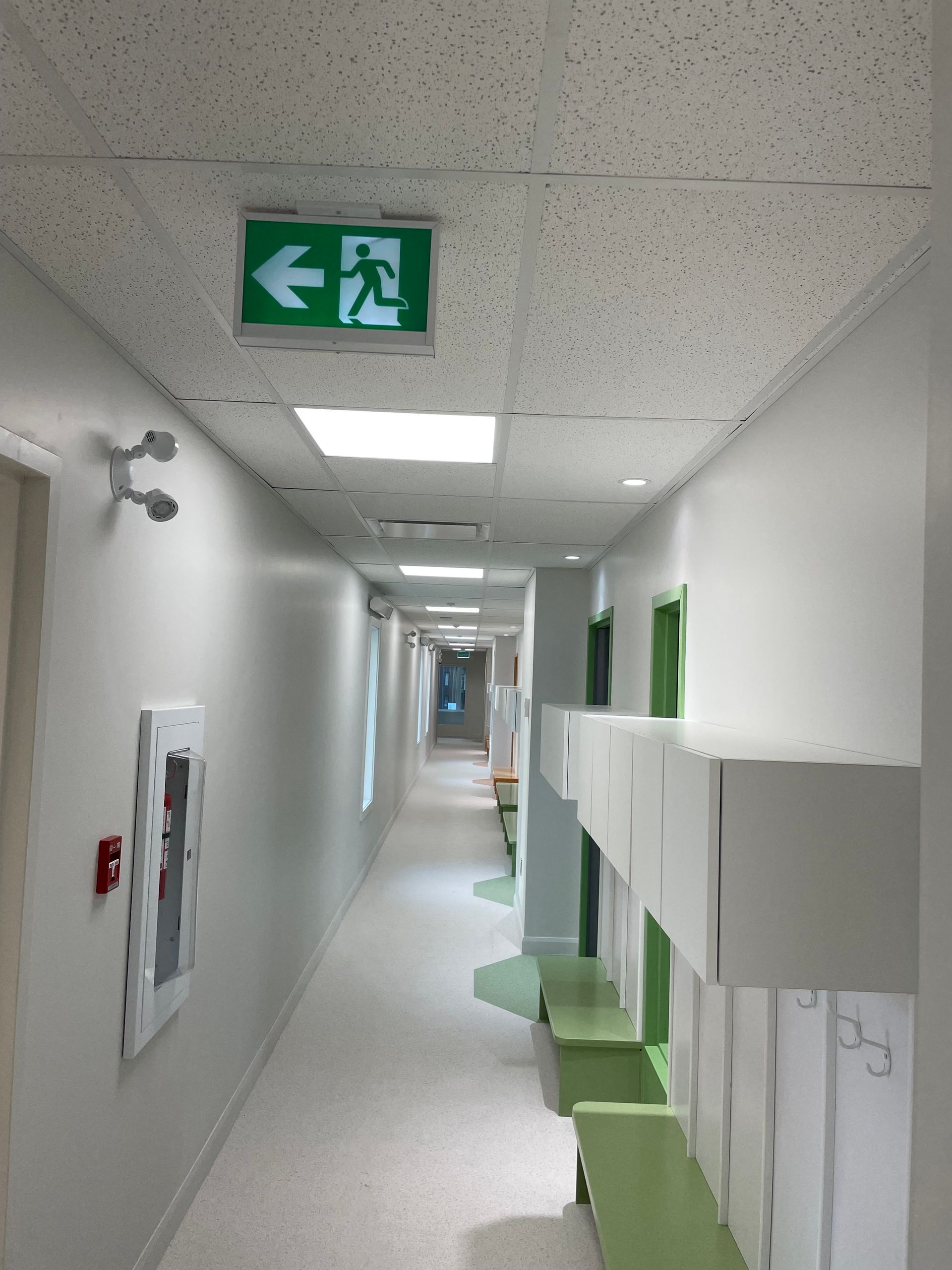 Un long couloir avec un panneau de sortie vert au plafond