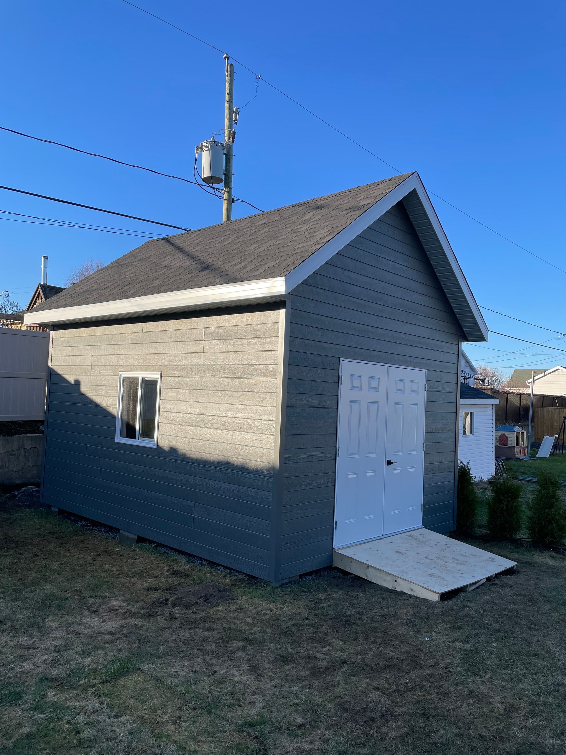 Un petit hangar avec un toit gris et des portes blanches