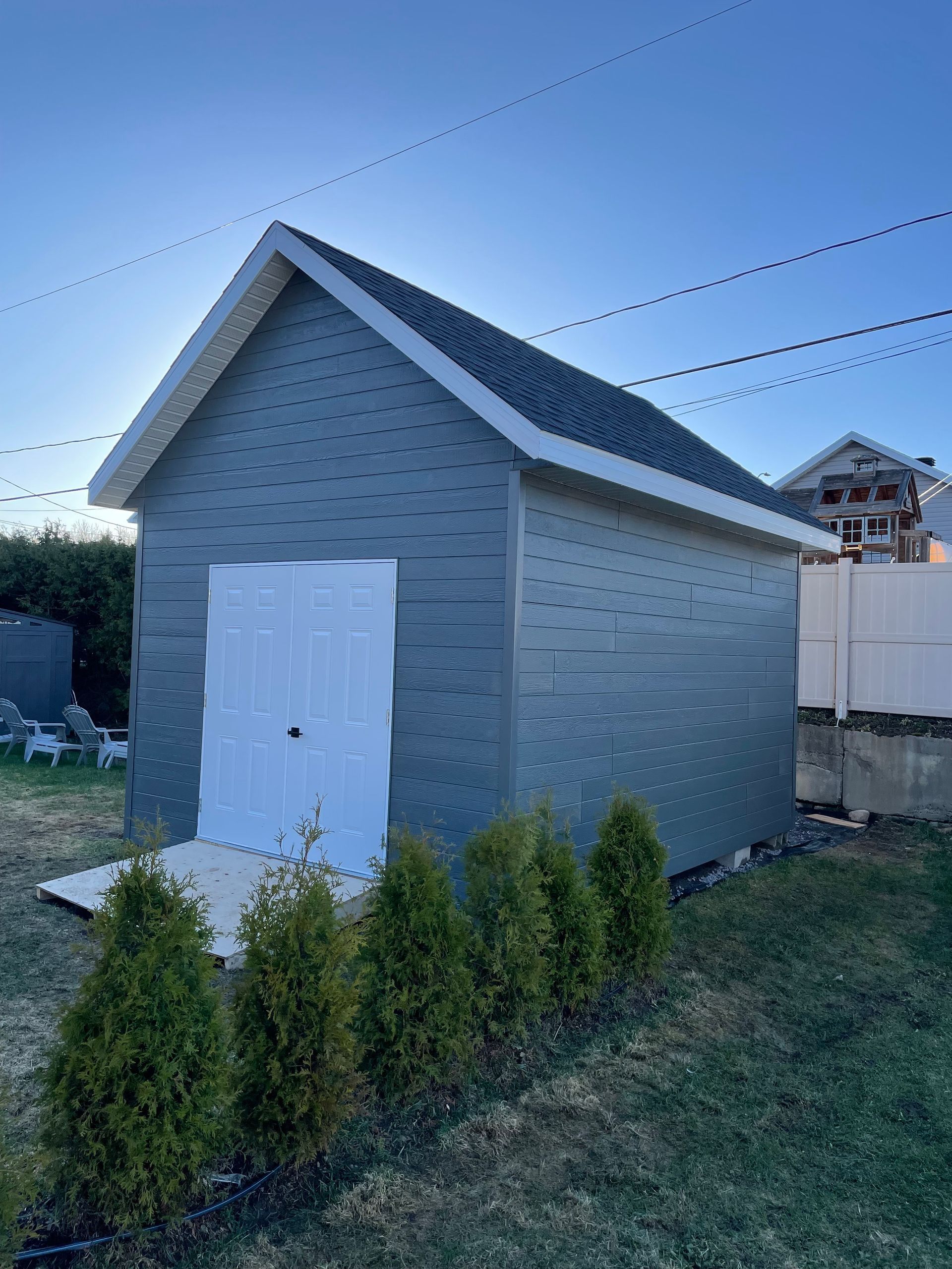 Un petit hangar avec une porte blanche se trouve au milieu d'une cour.