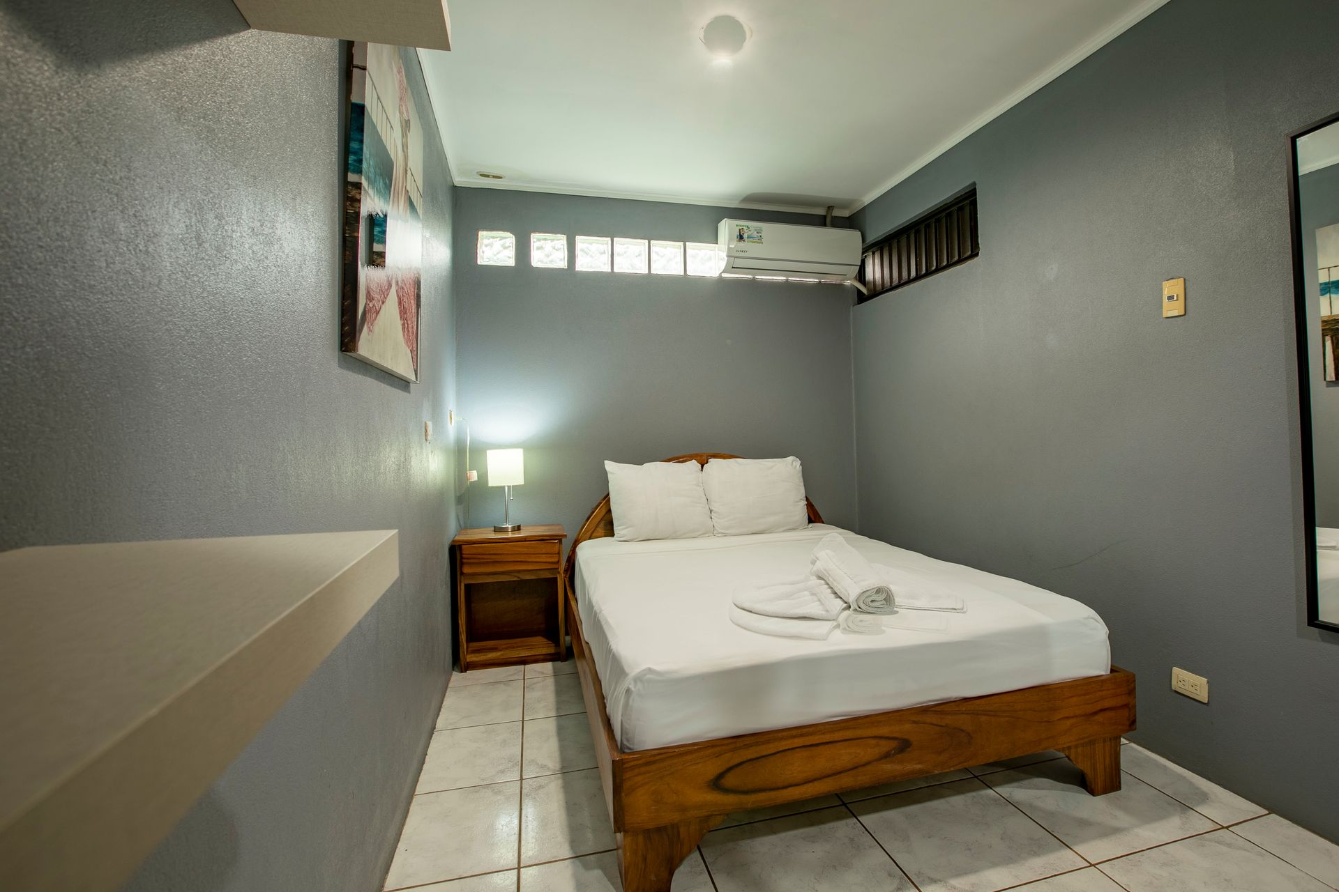 a bedroom with a bed , nightstand , mirror and air conditioner .