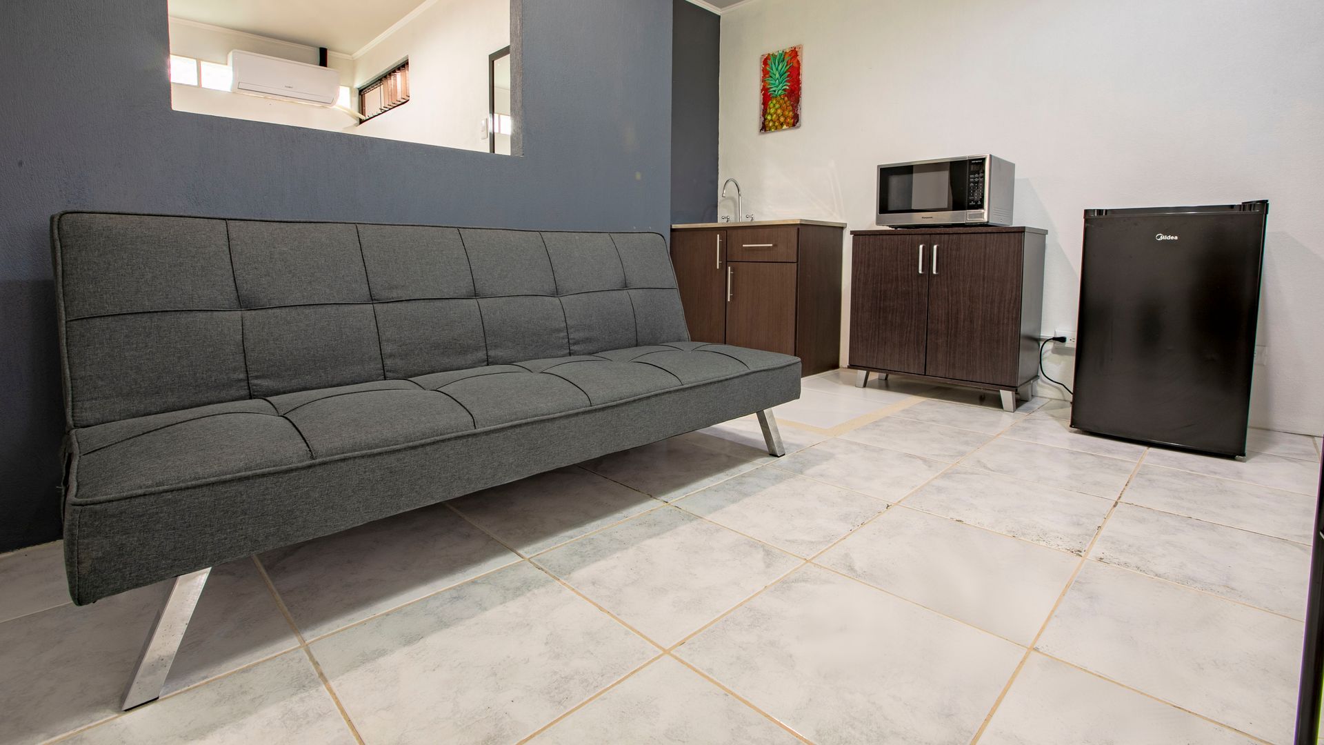 a living room with a couch , cabinets , a microwave and a small refrigerator .