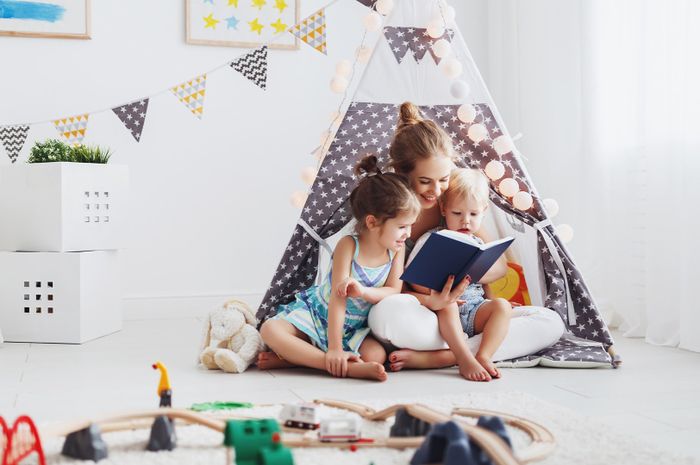 family mother reading to children book in tent in playroom at home