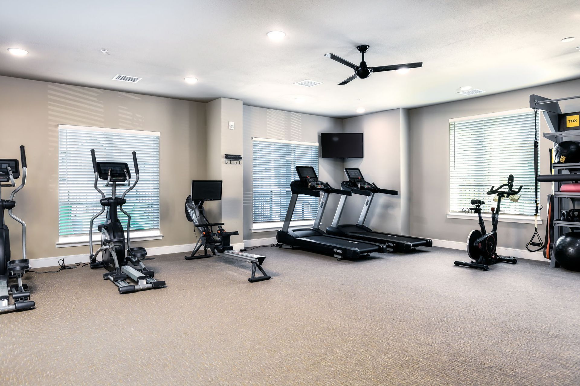 A gym with treadmills , exercise bikes , and a ceiling fan.