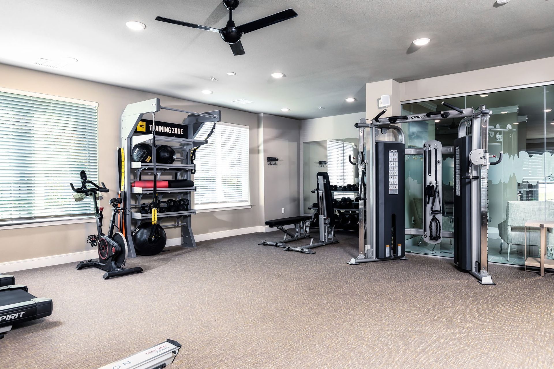 A gym with a lot of equipment and a ceiling fan