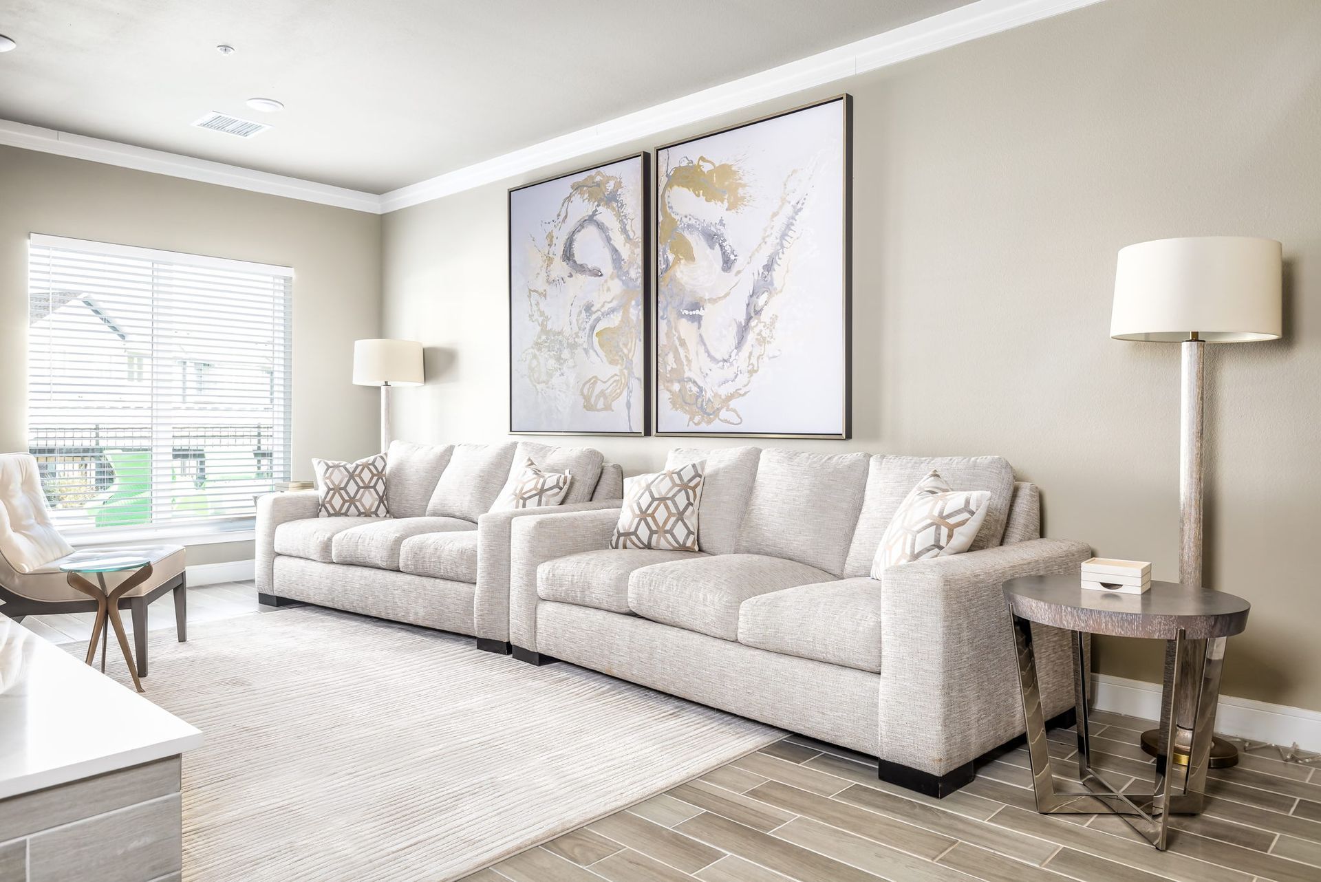 A living room with a large couch , two chairs , a table and two paintings on the wall.