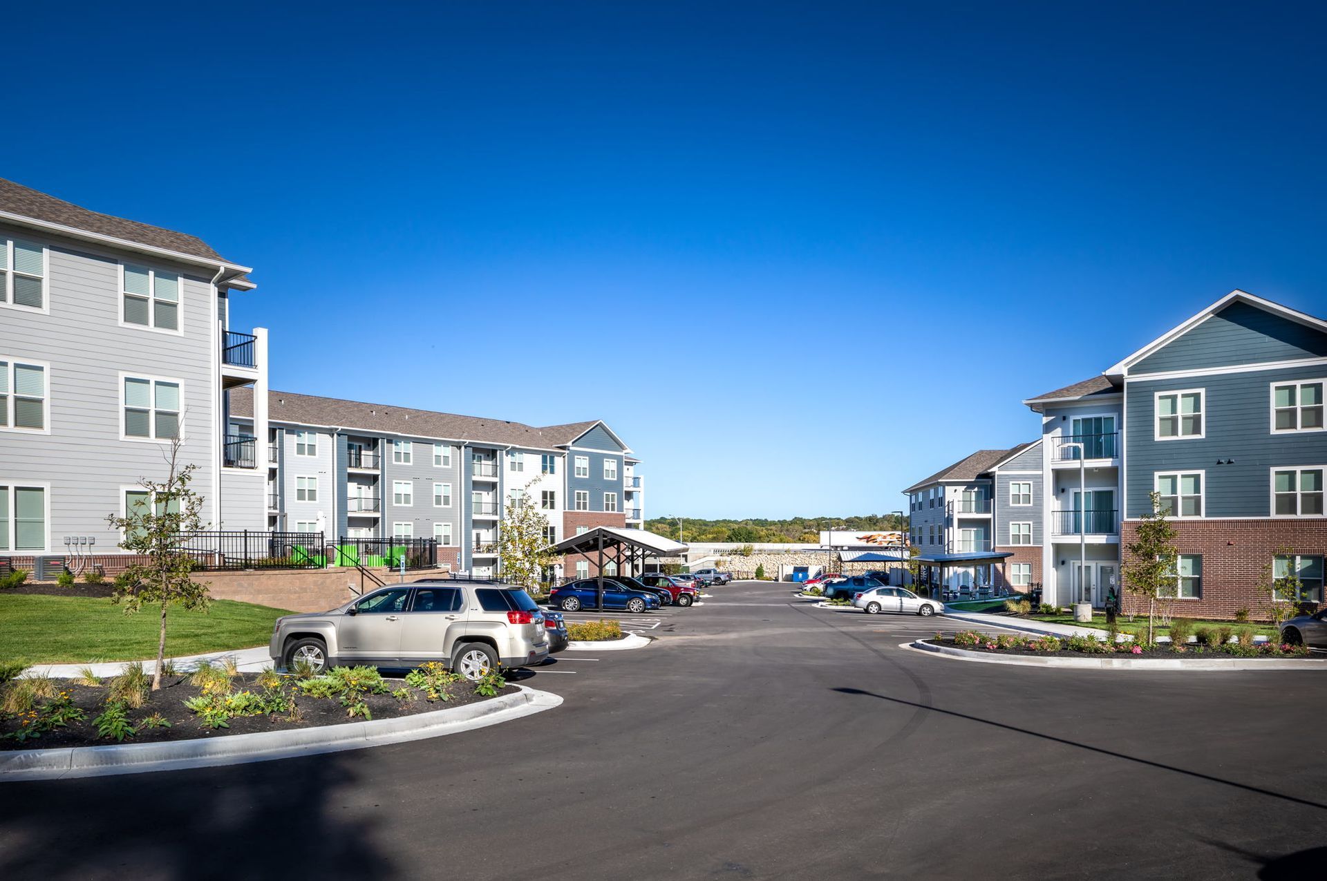 A row of apartment buildings with cars parked in front of them on a sunny day.