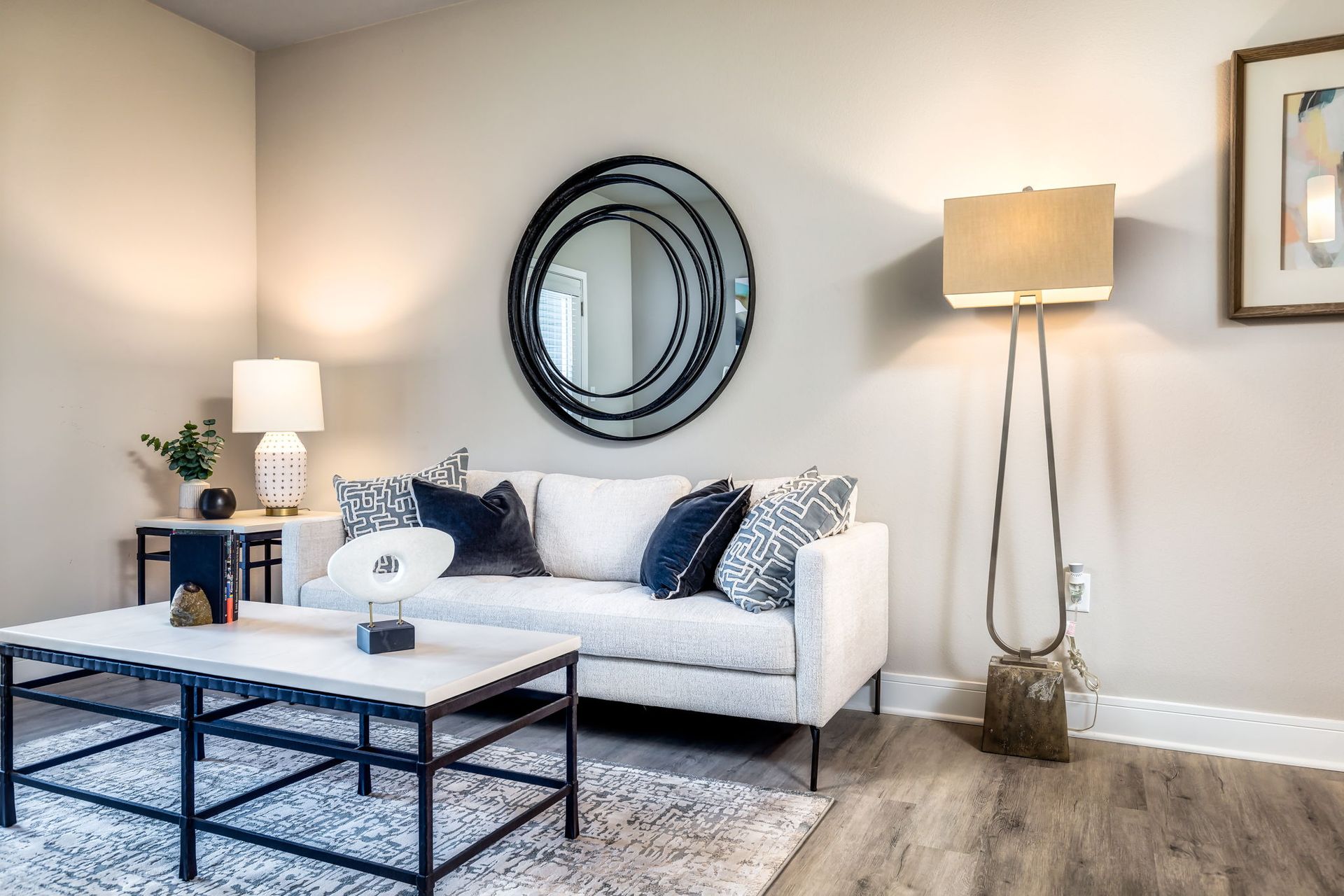 A living room with a couch , coffee table , lamp and mirror.