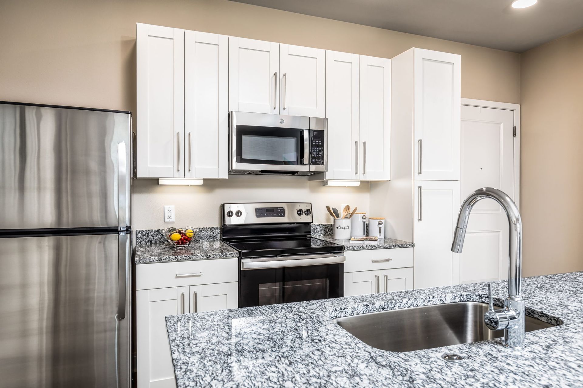 A kitchen with granite counter tops , stainless steel appliances , white cabinets and a sink.