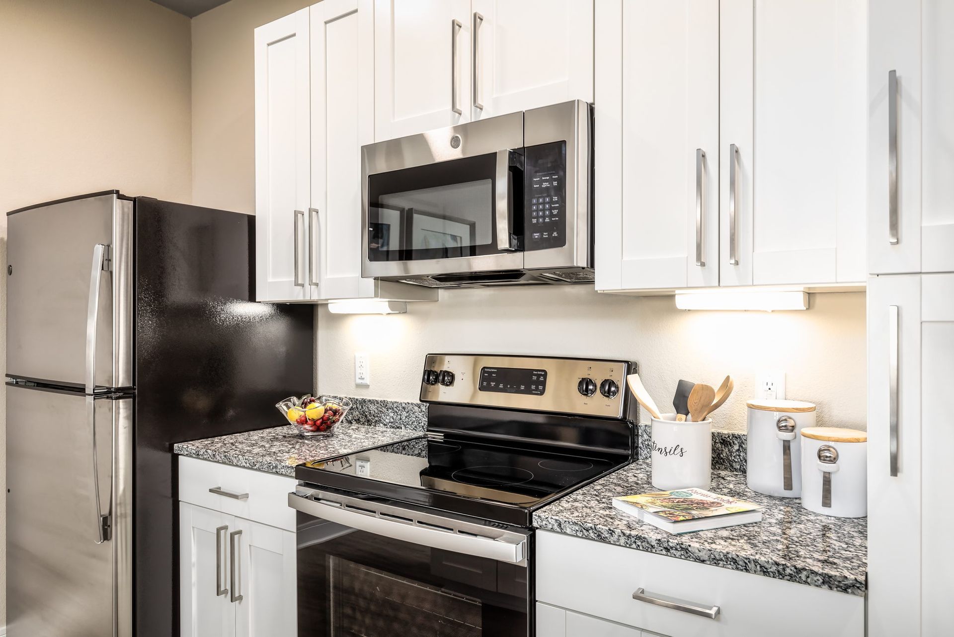 A kitchen with stainless steel appliances , granite counter tops , white cabinets and a black refrigerator.