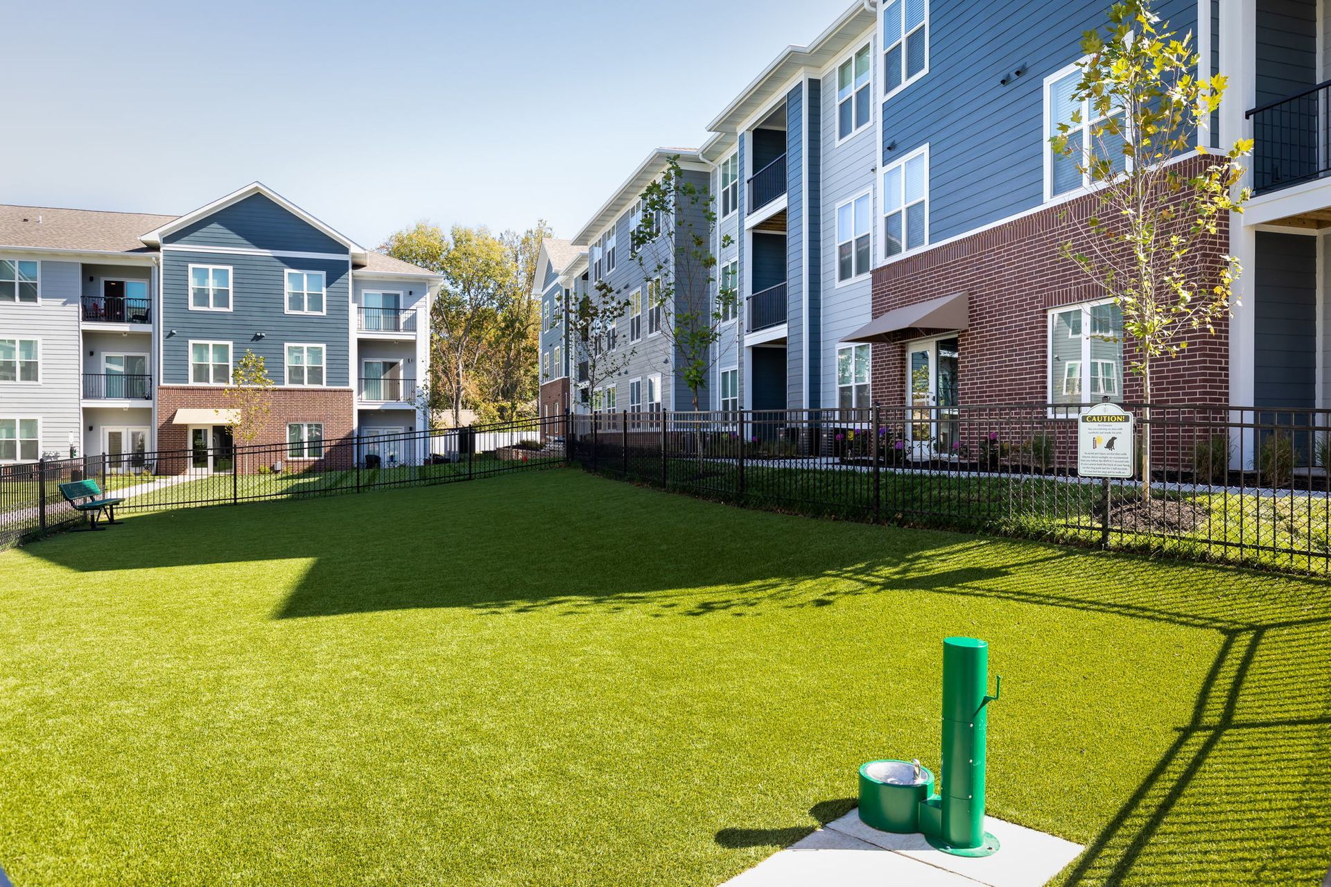 There is a dog park in front of a large apartment building.