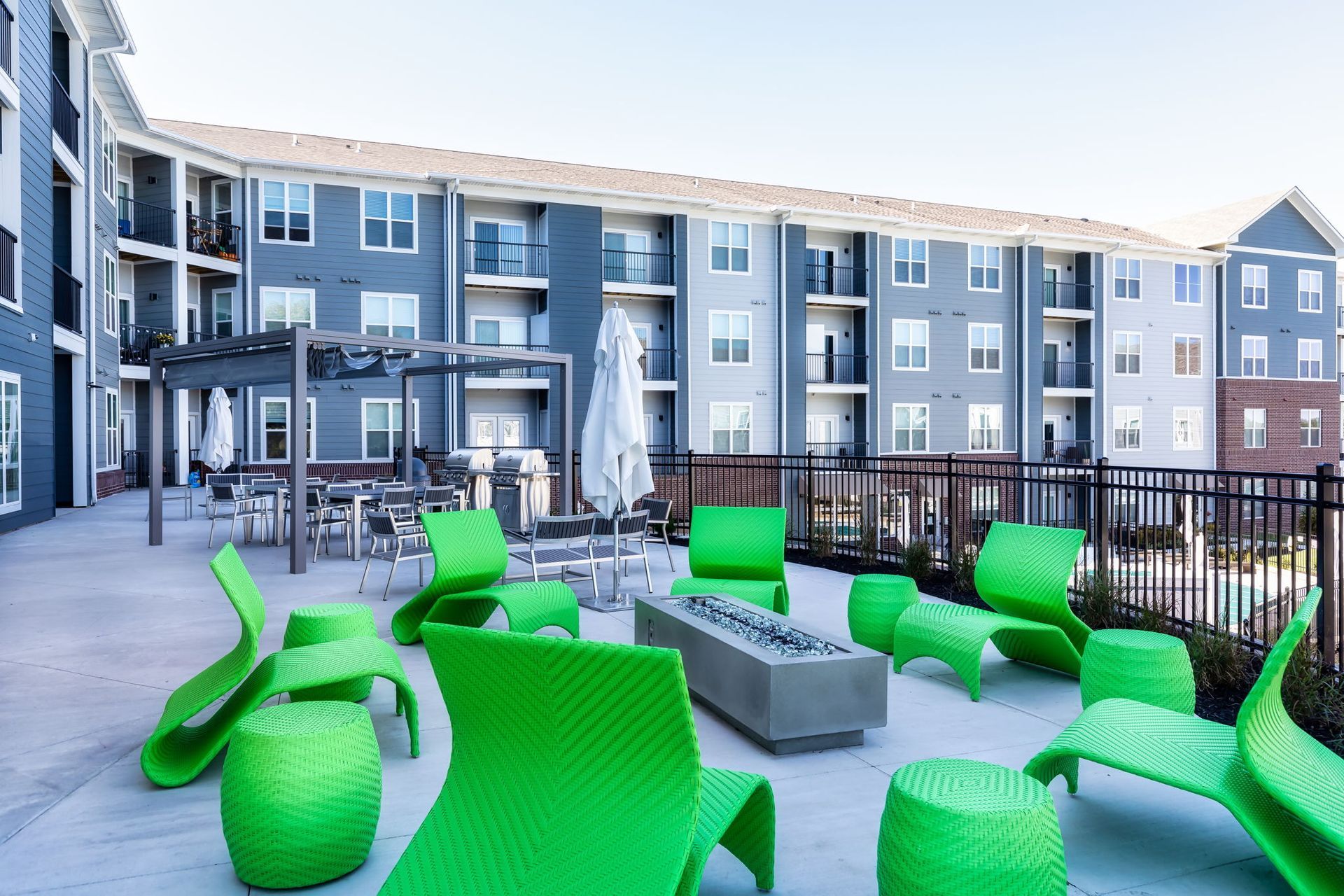 A patio with green chairs and a fire pit in front of a building.