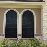 There are two arched windows on the side of a house.