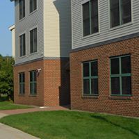 A brick building with green windows and a sidewalk in front of it.