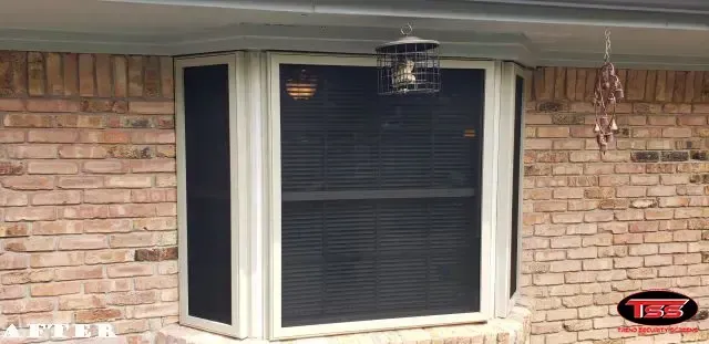 A window with a screen on it is on a brick wall.