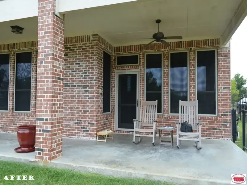 A brick house with a porch with rocking chairs and a ceiling fan