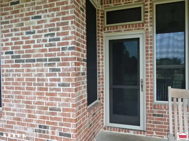 A brick porch with a screen door and a chair