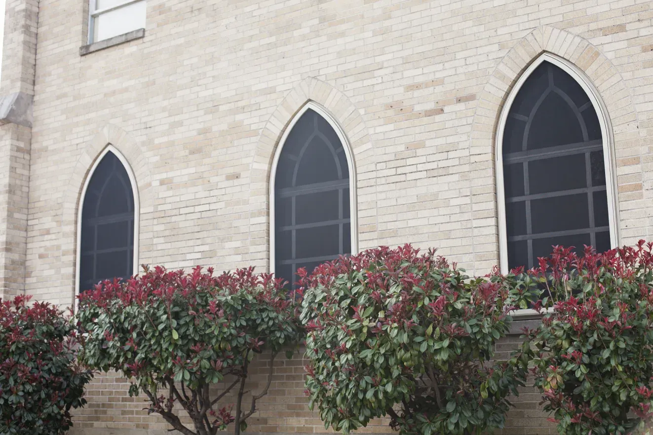 A brick building with arched windows and bushes in front of it