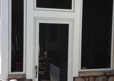 A screened in porch with a white door and two windows.