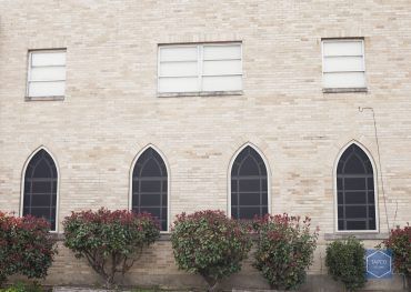 A brick building with arched windows and bushes in front of it