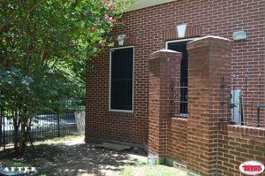 A brick building with two windows and a fence in front of it.