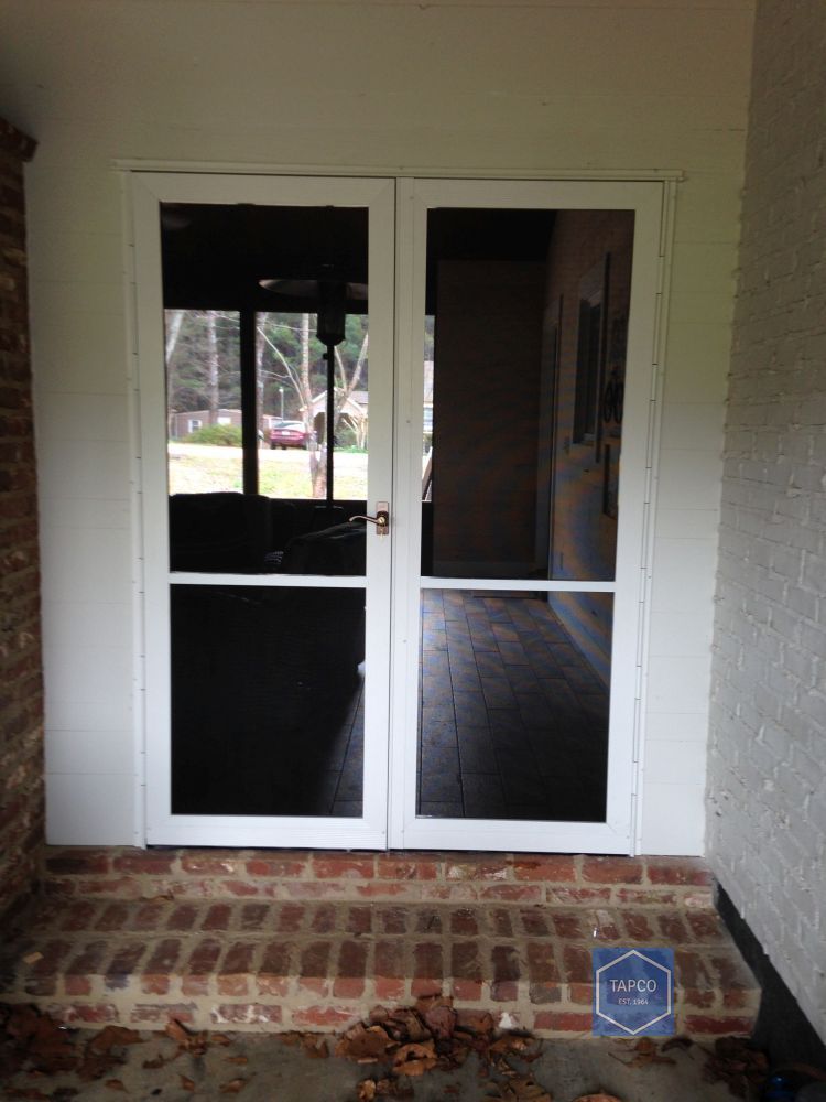 A white screen door is sitting on top of a brick porch.