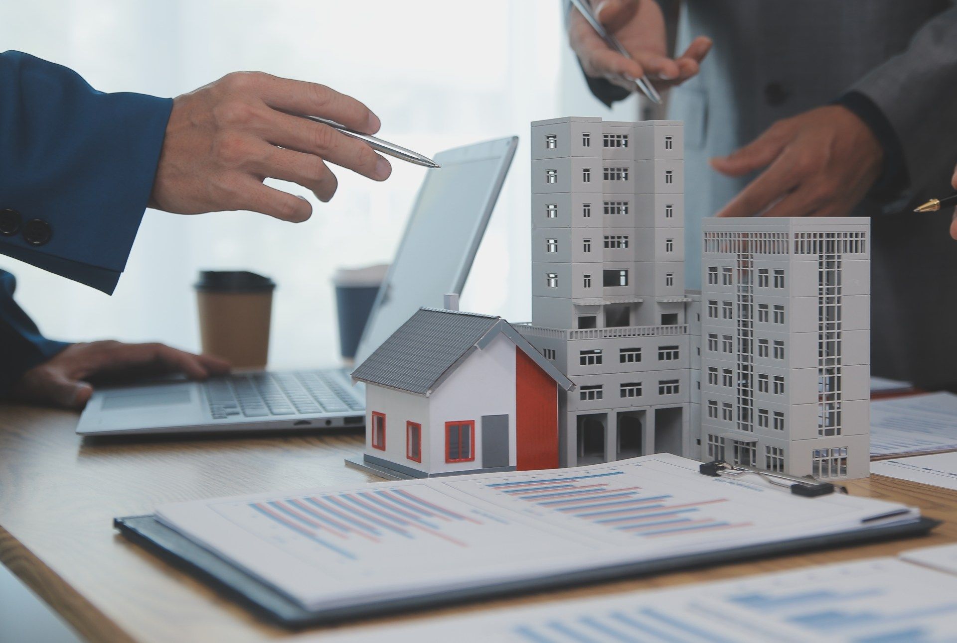 group of people are sitting at a table with a laptop and a model house.