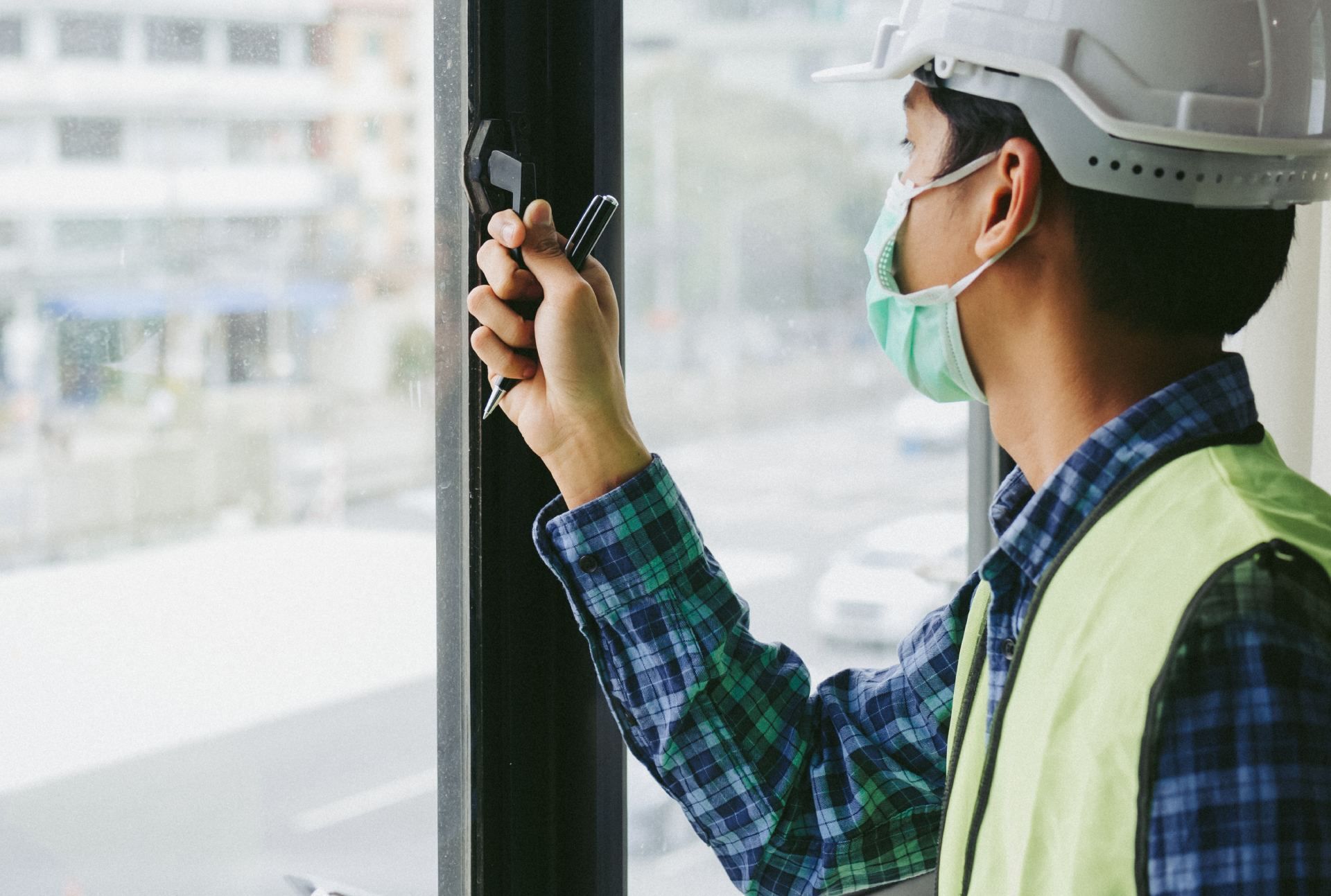 A construction worker wearing a mask and hard hat is working on a window.