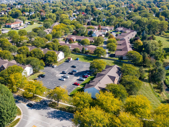 Aerial view of a suburban apartment complex with parking lots, trees, and surrounding roads