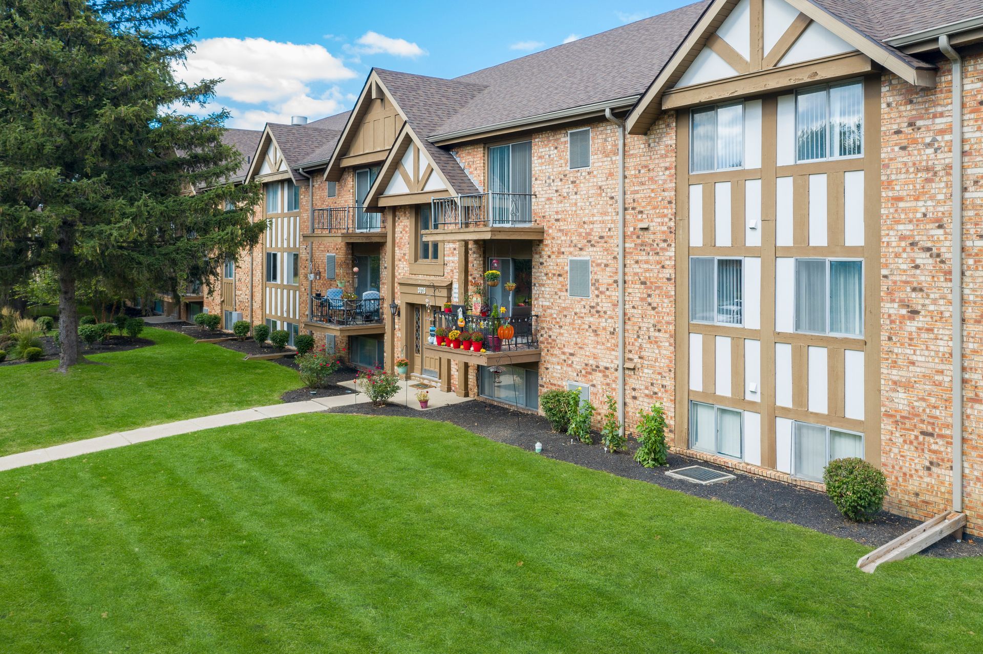 Brick apartment building with Tudor-style trim beside a green lawn and walkway