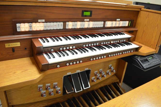 Wooden organ with three keyboards, foot pedals, and many buttons and switches.
