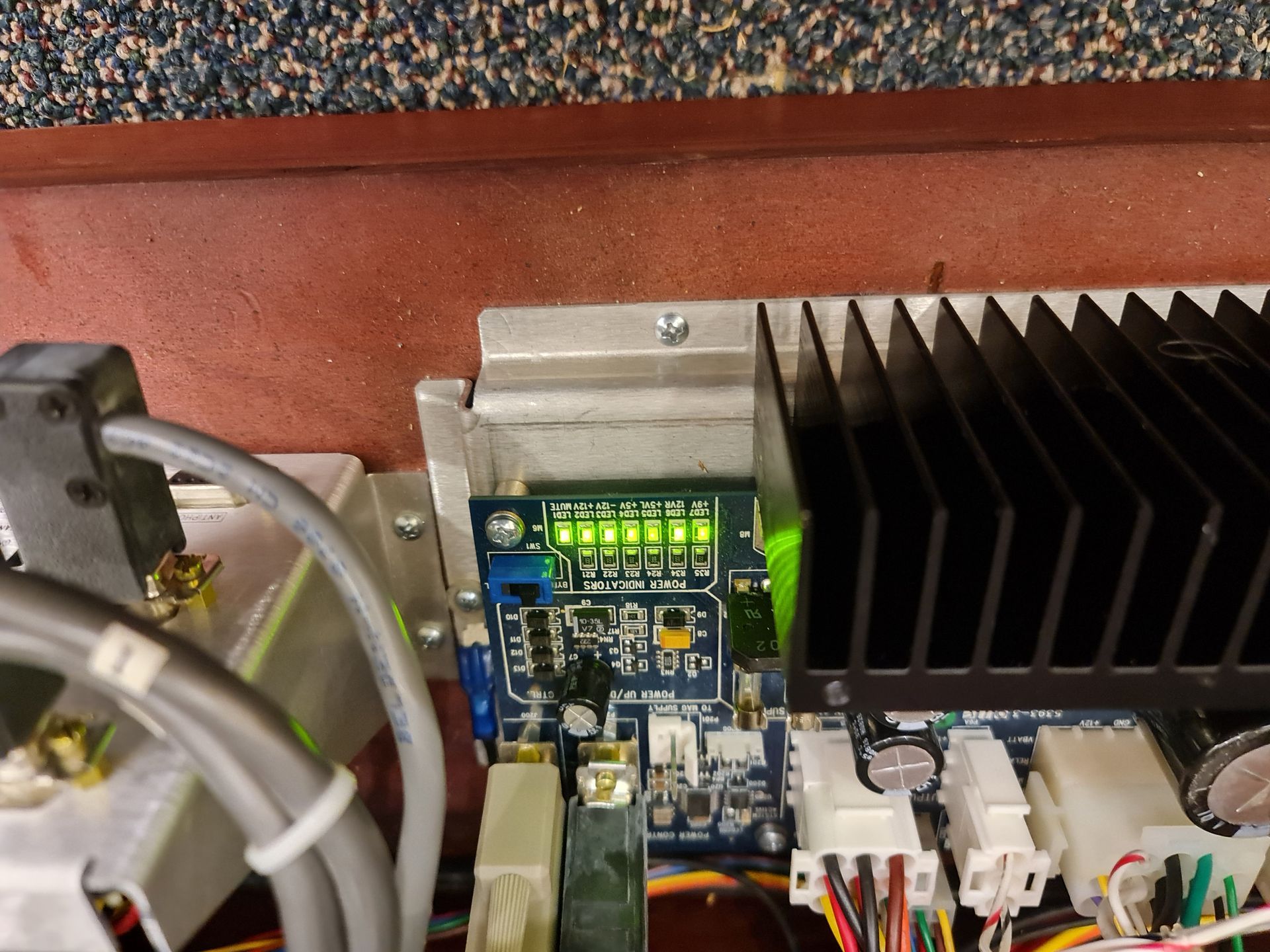 Circuit board with green lights illuminated, mounted on a metal heat sink in an electronic device.