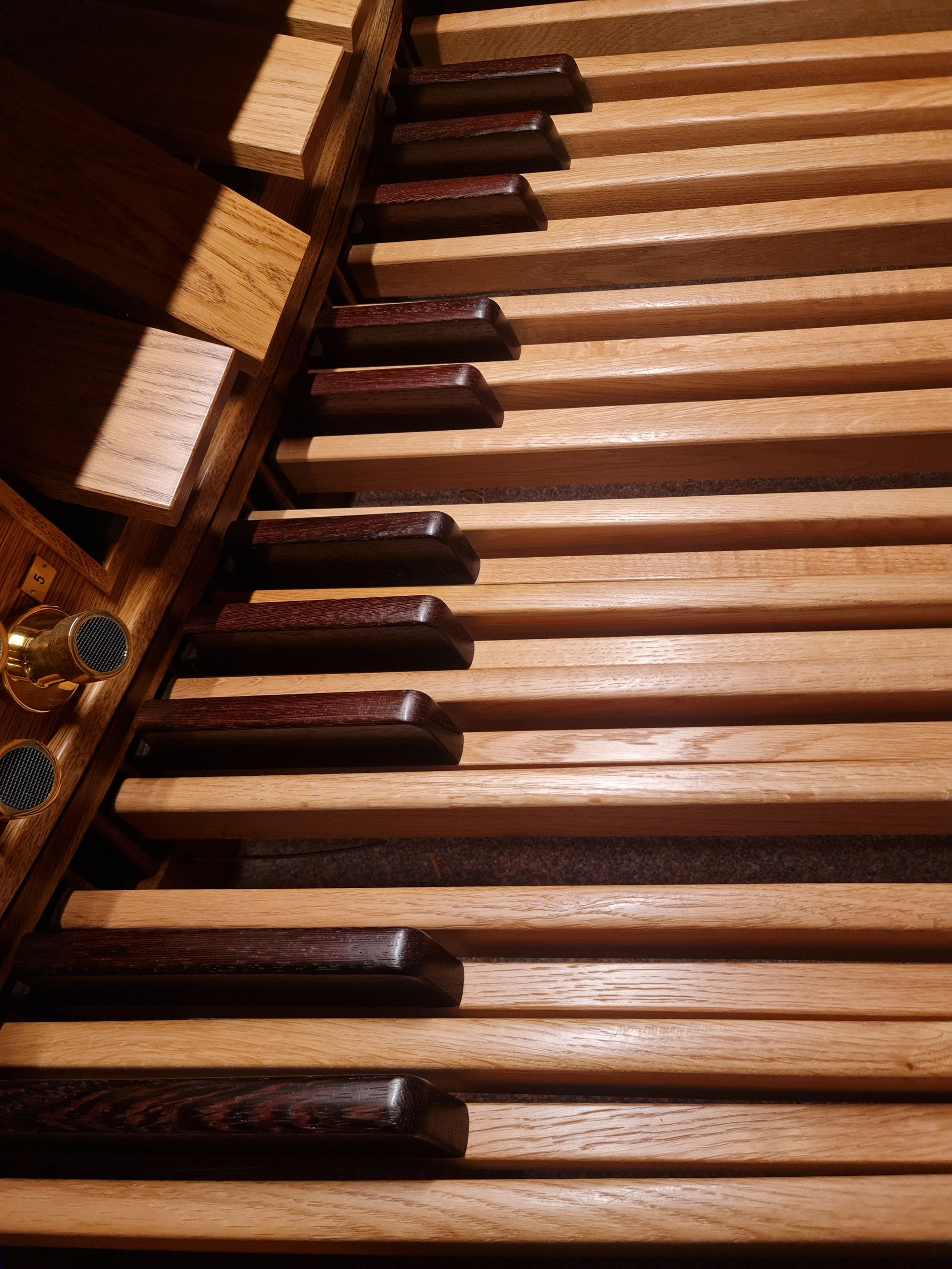 Close-up of a pipe organ's pedalboard. Wooden keys with dark brown tops and light brown spaces in between.