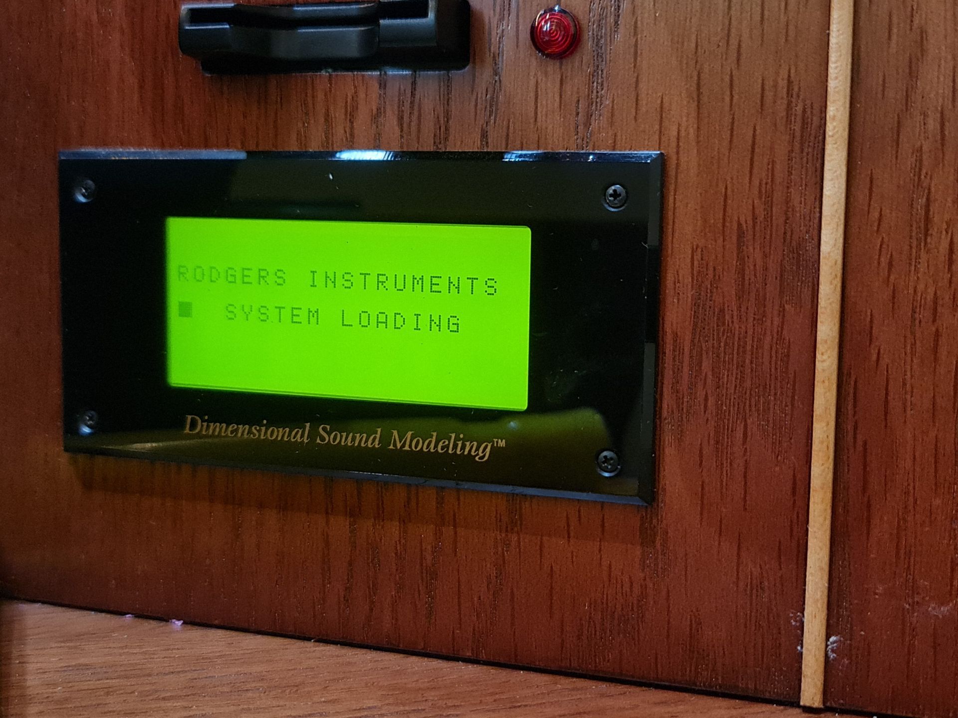 A wooden device with a green LCD screen displaying 