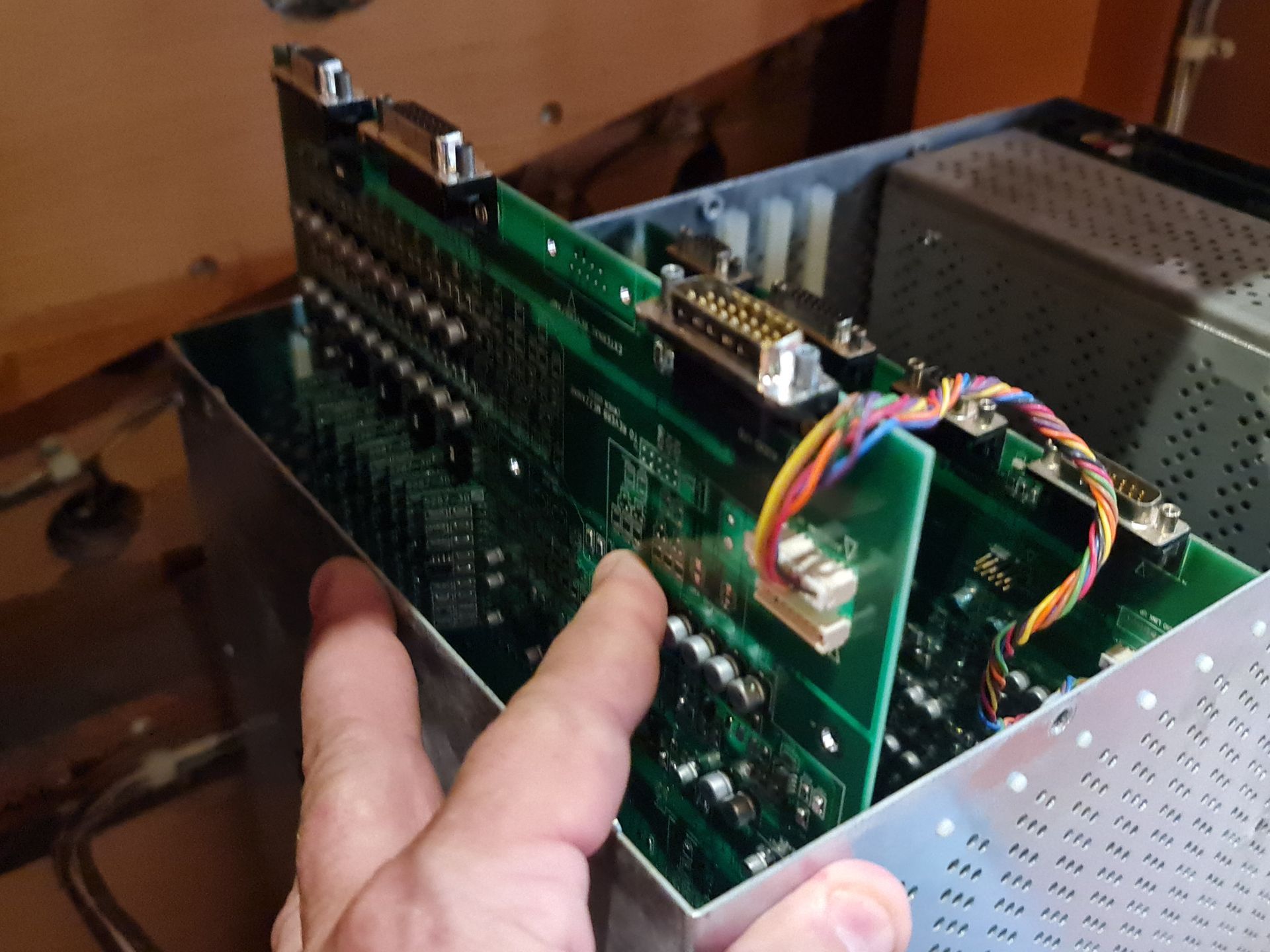 Person's hand touching circuit boards inside a metal chassis with multiple D-sub connectors.