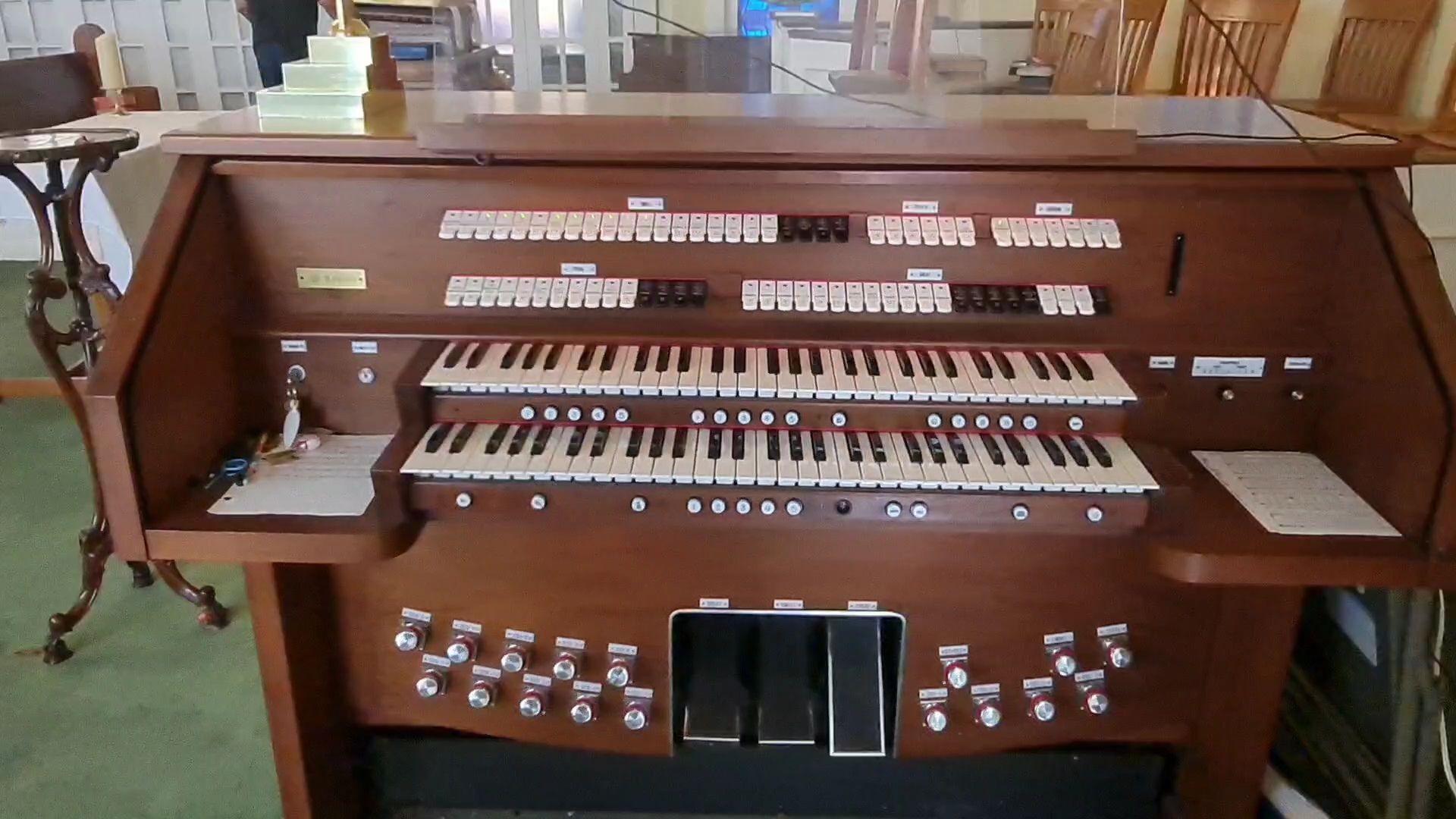 A brown church organ with multiple keyboards, buttons, and foot pedals.