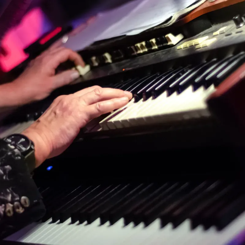 Hands playing a keyboard instrument, likely an organ, close-up with black and white keys.