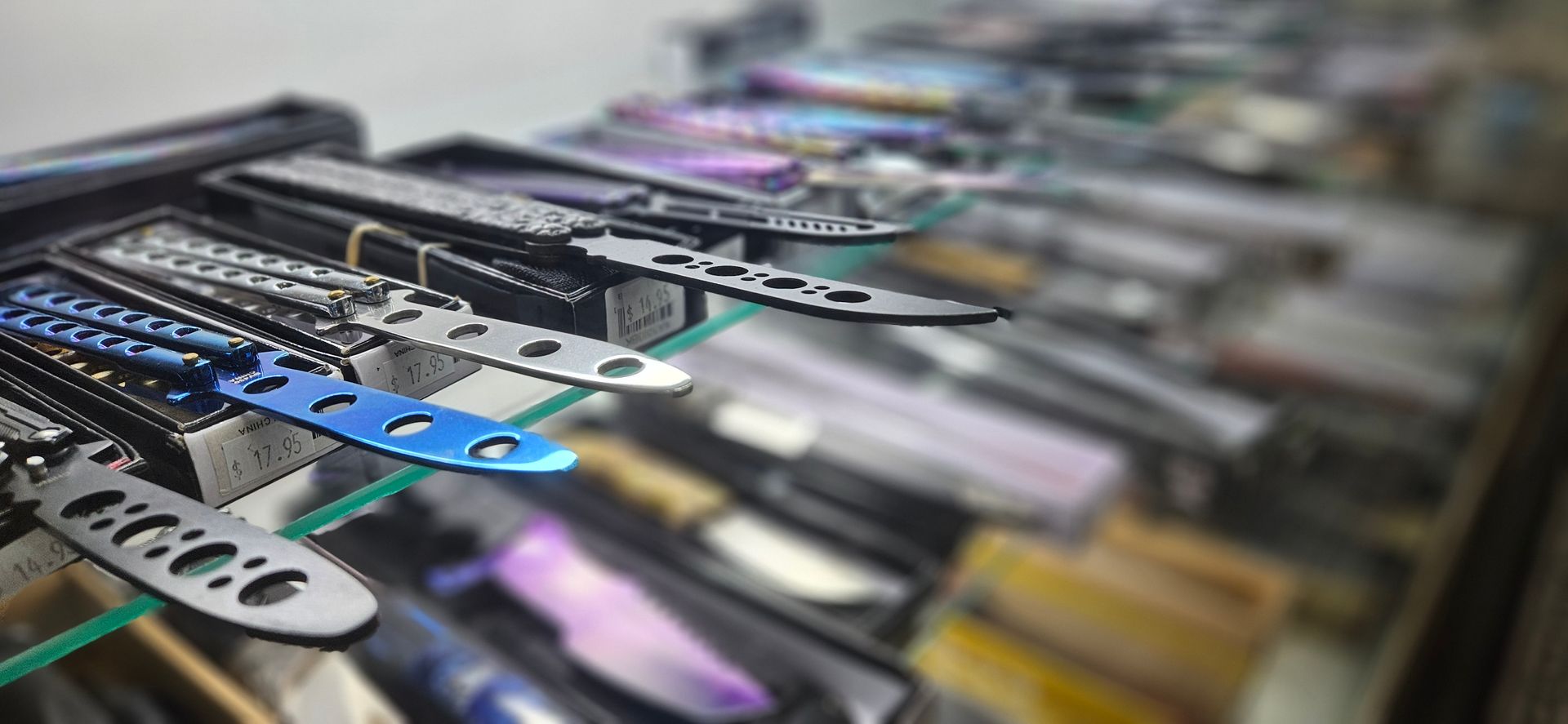 A case of knives  bokeh into the background showing blurry fixed blades and featuring balisong (butterfly knives) in focus. 