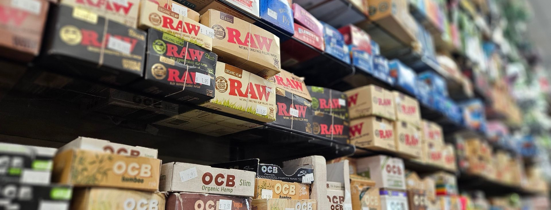 A veritable wall of rolling papers looms, showing OCB, Raw, Elements and other brands.