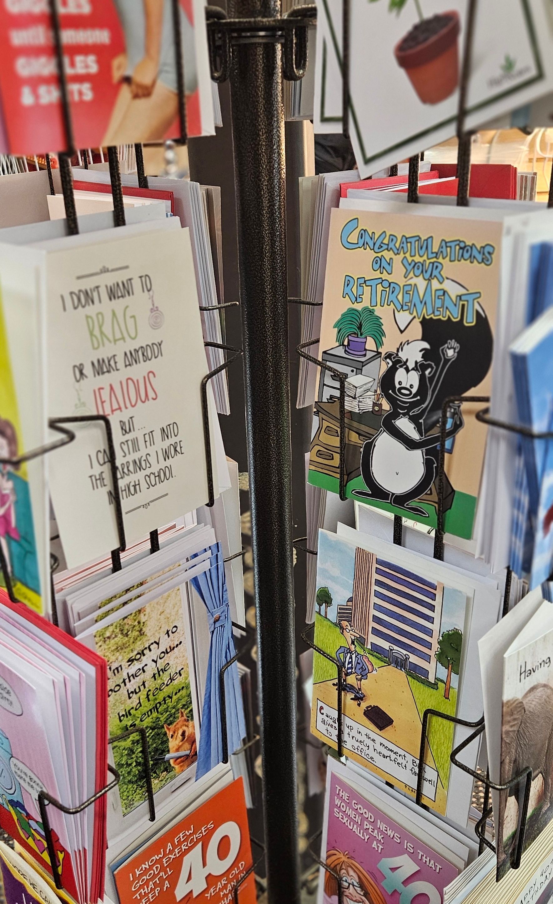A close up image of a card rack displaying a variety of card types. A retirement, birthday, valentines card are featured.
