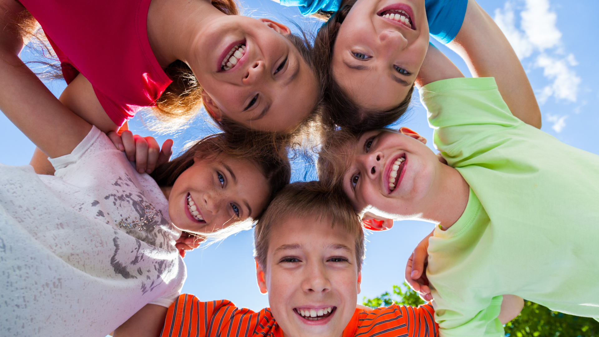 Group of children smiling and looking down, blue sky background.