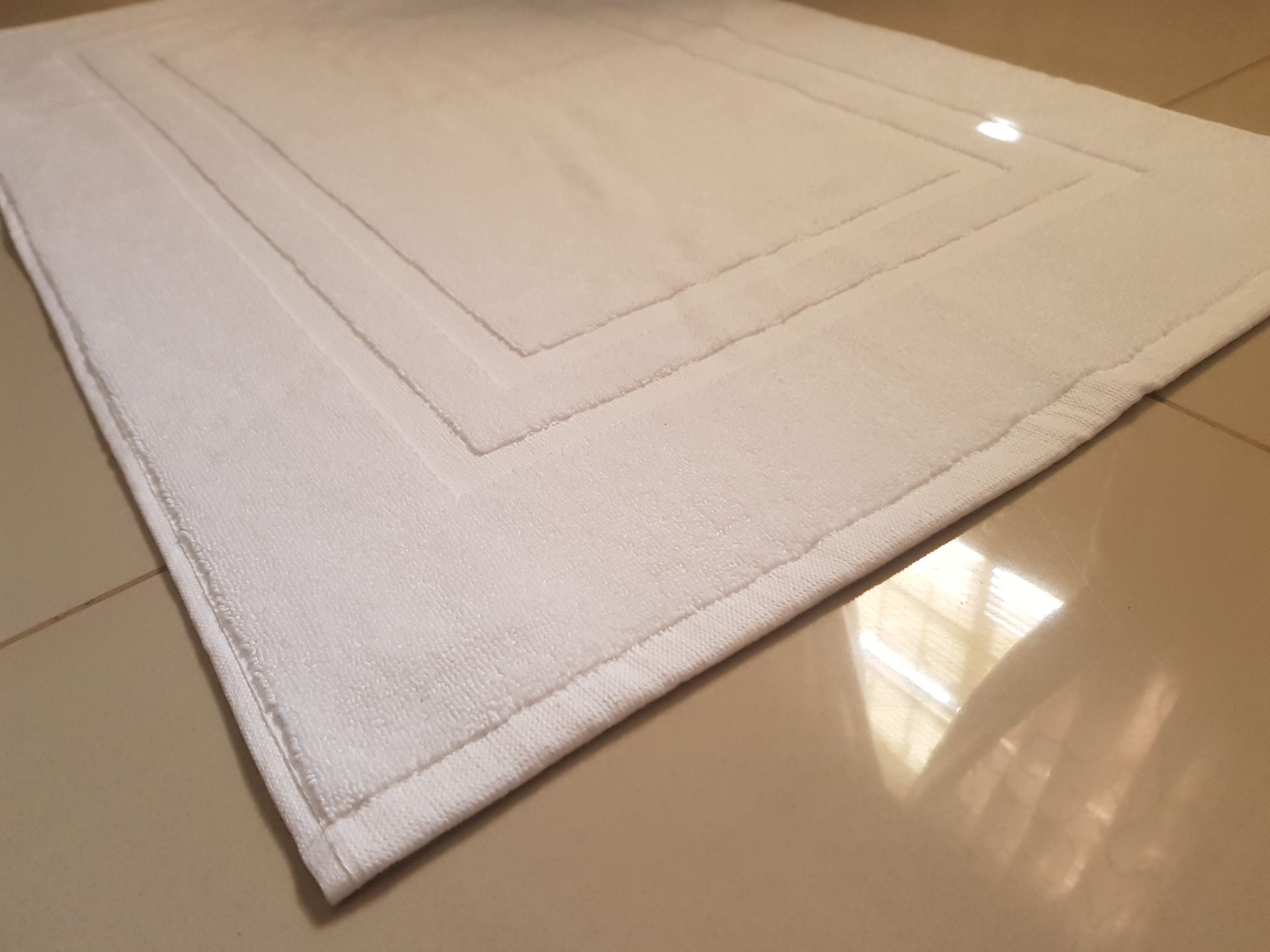 A bed with white sheets and pillows and a nightstand with a plant on it.