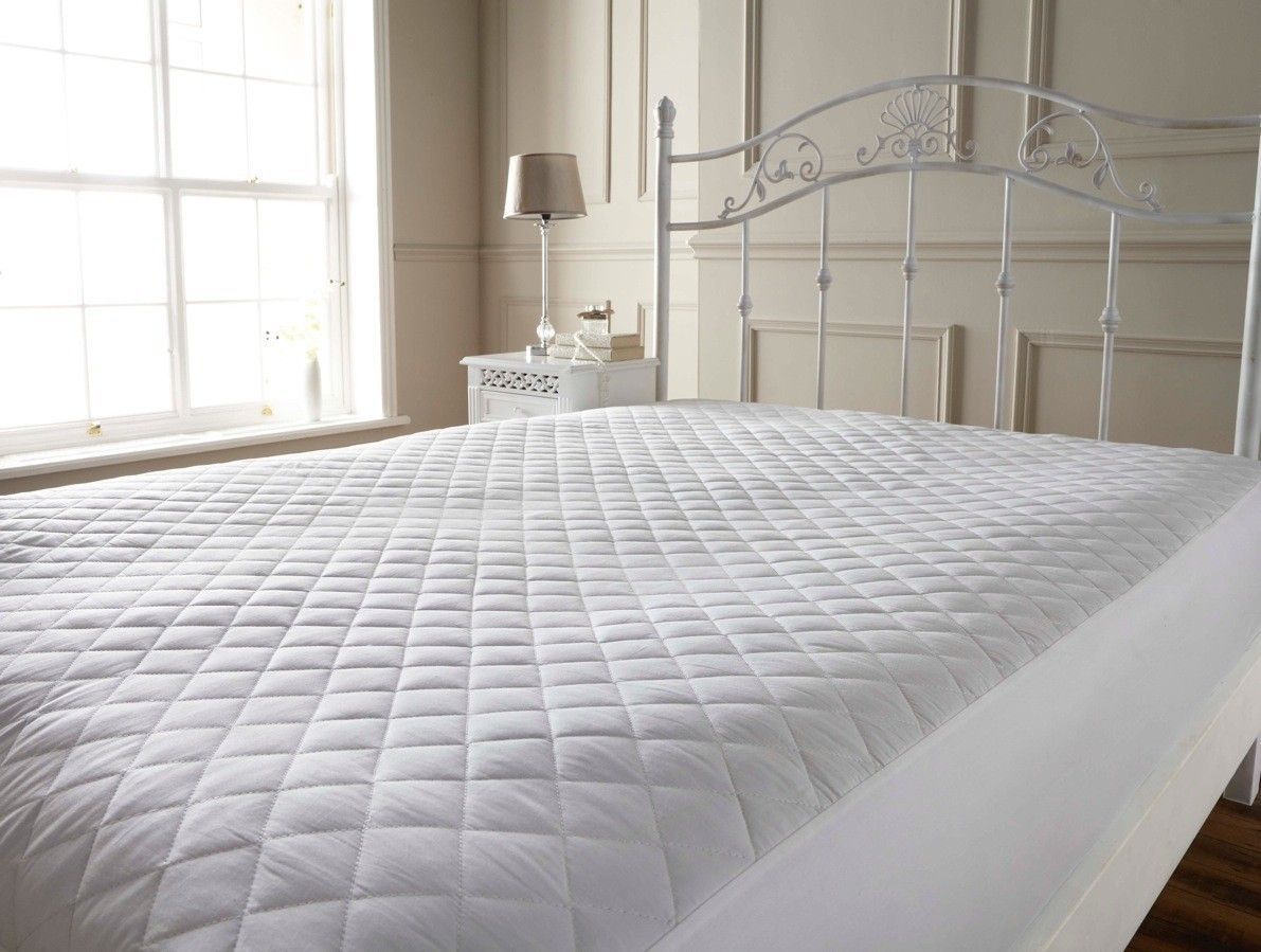 A bed with a white mattress protector on it in a bedroom.