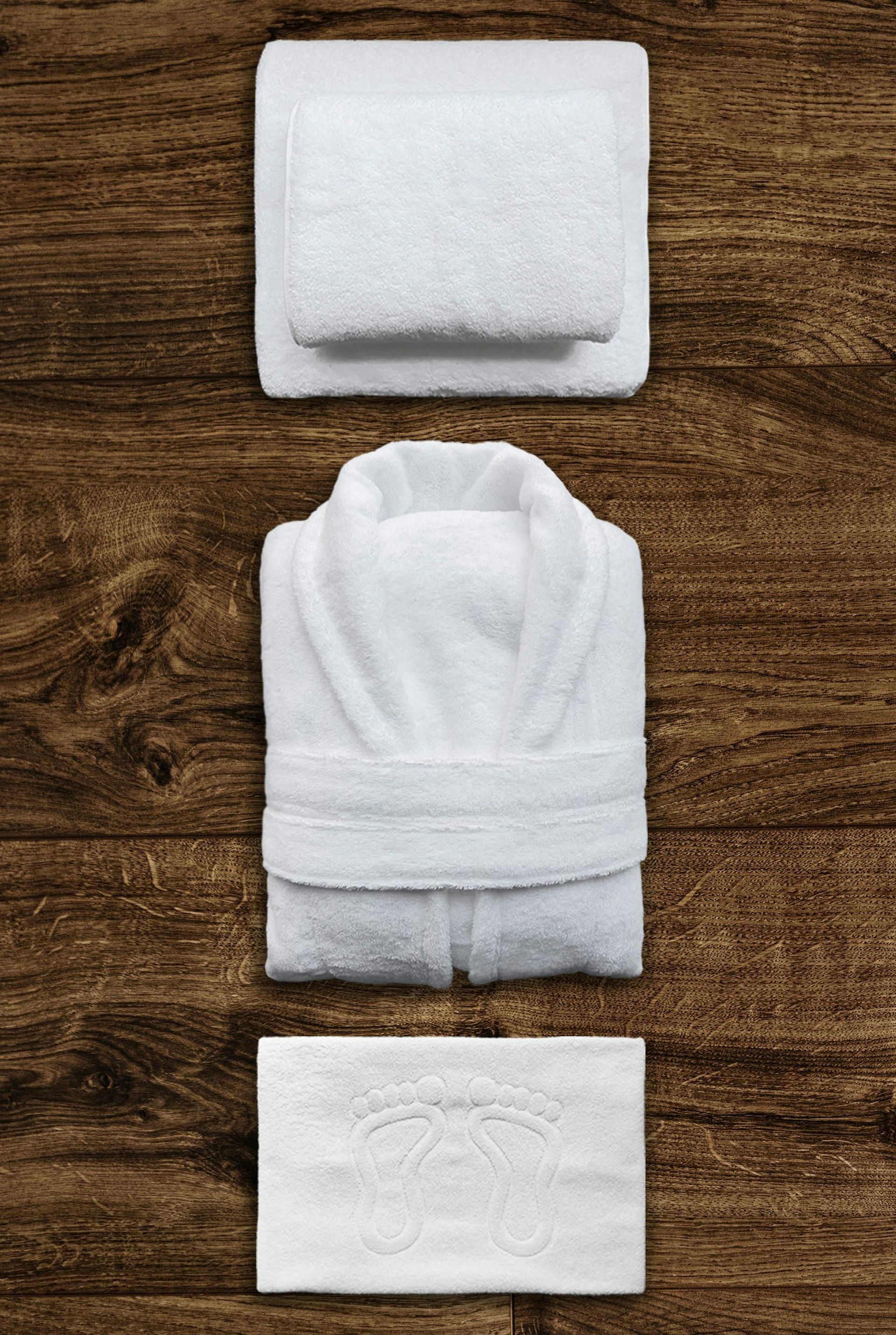 A white robe , towel , and soap are on a wooden table.
